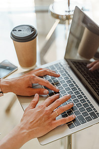 手在白色办公桌上的电脑键盘上打字，上面放着一杯咖啡和用品，顶视图。