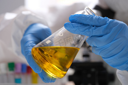 戴手套的化学家拿着装有黄色油状液体的试管，用于研究特写