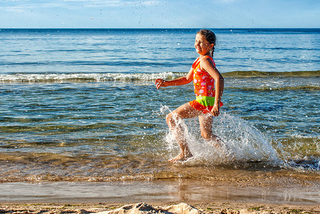 海边水花摄影照片_快乐的小女孩在海滩上溅起水花