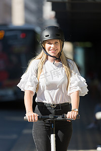 时髦时髦的少年，美丽的金发女孩在城市环境中骑公共租赁电动滑板车。
