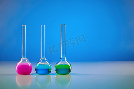 有五颜六色的化学试剂的三个医疗烧瓶为测试，蓝色背景。