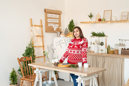 圣诞毛衣摄影照片_穿着圣诞毛衣的快乐年轻女人在厨房里做热饮