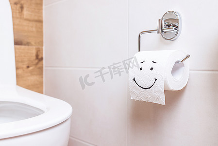 挂着的包摄影照片_浴室的白墙上挂着一卷卫生纸，上面挂着一张幸福的脸