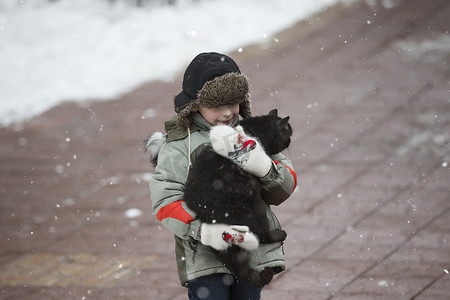 一个戴着裘皮帽的男孩和一只无家可归的猫