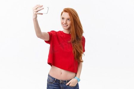 白墙背景中孤立的年轻快乐红发女性的形象使自拍看起来像相机