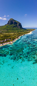 le摄影照片_Le Morne 海滩毛里求斯，带棕榈树和白色沙滩蓝色海洋的热带海滩和带雨伞的沙滩床、太阳椅和遮阳伞在热带海滩的棕榈树下，Le Morne 海滩毛里求斯
