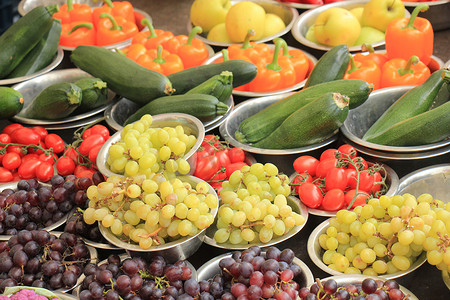 小摊位摄影照片_市场摊位上的新鲜水果和蔬菜：小金属碗中展示的葡萄、西红柿、西葫芦和辣椒