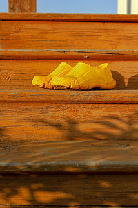 夏日生活场景摄影照片_夏日后院旧橙色楼梯上的黄色橡胶泥泞工作鞋，日落时分，乡村和乡村正宗的心情