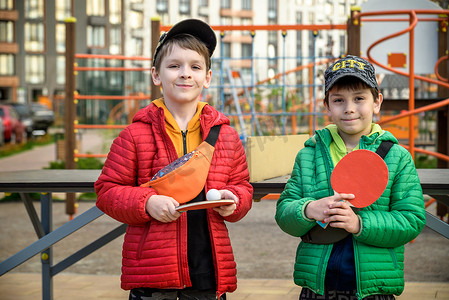 孩子的手图标摄影照片_两个快乐的男孩，十几岁的双胞胎兄弟，在户外享受假期打乒乓球。