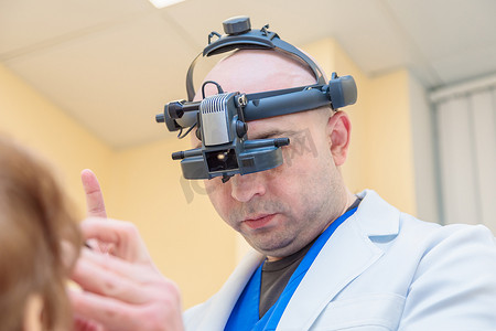 眼科诊断摄影照片_男性眼科医生用双目检眼镜检查成年女性的视力