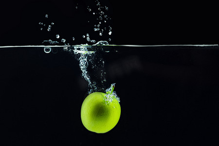 溅起水花摄影照片_青苹果落入水中，深色背景下溅起水花