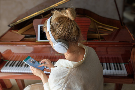 戴耳机的小女孩弹古董钢琴，用智能手机学习