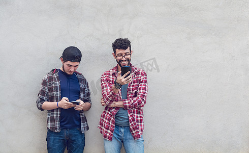 两个男士摄影照片_微笑的家伙检查他们的手机，微笑英俊的年轻人检查他们的手机，两个家伙享受他们的手机