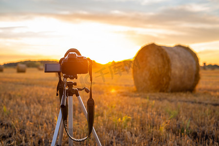 三脚架上的相机准备在夏末田野里拍照，日落时上面有许多稻草球