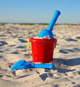 红色塑料桶和蓝色耙子，沙子上的铲子