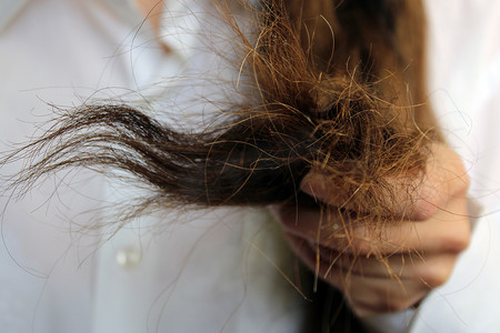 浴室吹头发外模摄影照片_女孩手里拿着受损干燥的头发。