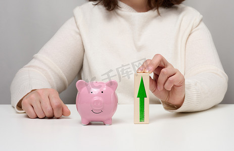 粉色陶瓷存钱罐和带有向上箭头的木块。