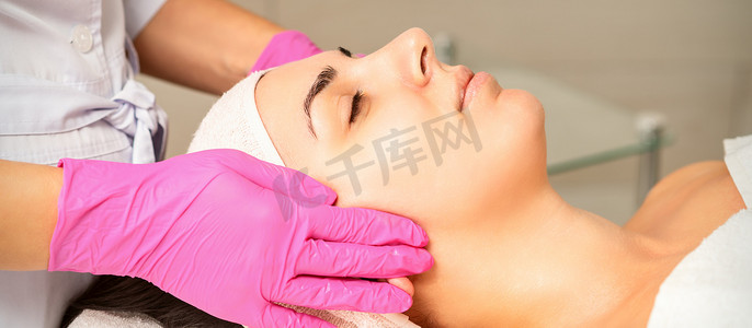 保湿面膜摄影照片_戴着手套的美容师在女性脸上涂上带去角质霜的保湿面膜。