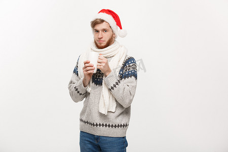 圣诞节概念 — 穿着毛衣和圣诞老人​​帽子的年轻胡子男子拿着一个热咖啡杯，用白色隔开，上面有复制空间。
