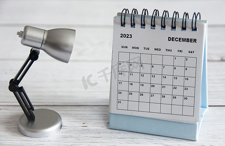 2023年年会摄影照片_2023 年 12 月白色台历，木桌上有台灯。