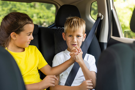 快乐的孩子，可爱的蹒跚学步的女孩和十几岁的弟弟坐在现代汽车里，锁着安全带，享受夏季周末的家庭度假旅行