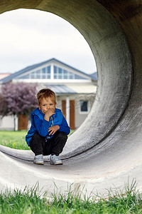 一个穿着蓝色背心的可爱孩子蹲在混凝土隧道里思考着什么。