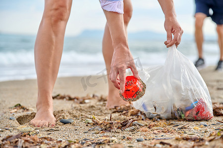 一个女人的手把塑料垃圾捡到沙滩上的袋子里的特写
