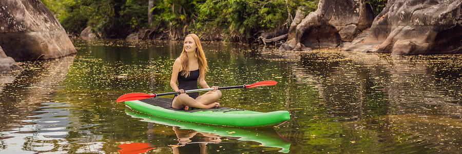 女孩长图摄影照片_SUP 站起来桨板女人在湖上桨板快乐地站在蓝色水面上的桨板上。