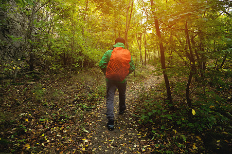 一位身穿绿色夹克和红色背包的游客在春天或秋天沿着山间小道行走。