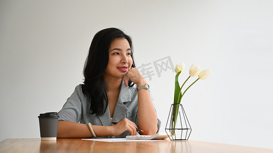 自信的女商人坐在个人办公室里，望着窗外，梦想着未来新的成功项目