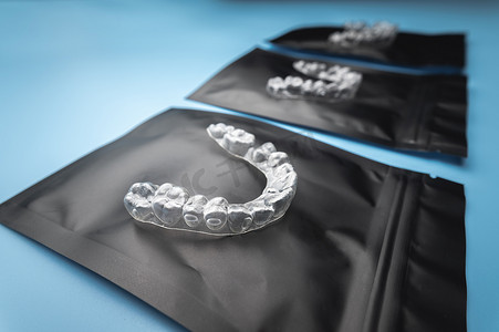 新的透明塑料牙套位于一个特殊的正畸包装上，蓝色背景上有拉链，工作室拍摄，无人