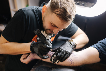 纹身师摄影照片_纹身师正在给一个男人的手纹身。