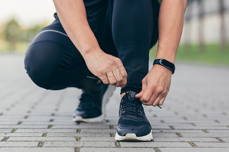 亚洲男运动员在慢跑前把鞋带系在运动鞋上，在公园里跑步