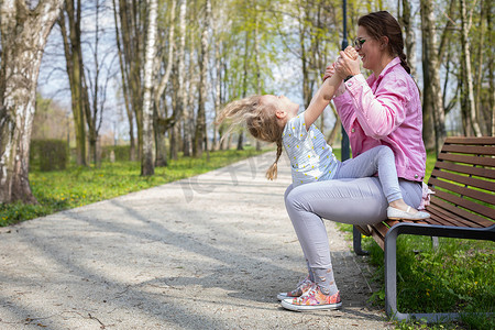 一位母亲坐在城市公园的长凳上，上下抱着女儿。