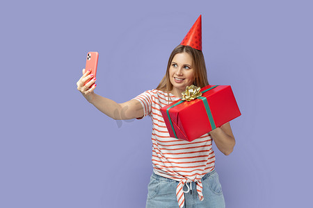 生日会主kv摄影照片_派对锥中的女博主拿着礼物盒自拍或进行视频通话。