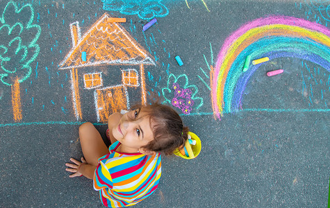 彩虹上的儿童摄影照片_孩子用粉笔在柏油路上画了一栋房子和一条彩虹。