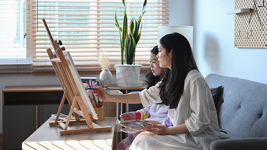 彩活动摄影照片_两个可爱的亚洲女孩在画架上用水彩画画。