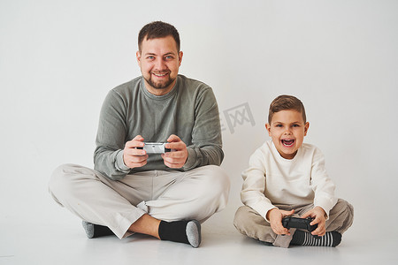 游戏手柄摄影照片_儿子和爸爸用游戏手柄玩游戏机游戏。