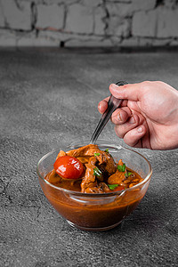 马志摄影照片_灰色背景透明碗里放着肉、蘑菇、西红柿的汤。