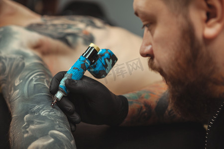 纹身师摄影照片_大胡子纹身师在他的客户身上纹身