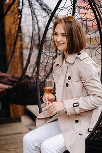 一个穿着灰色外套的快乐时尚女孩坐在外面的扶手椅上喝着饮料