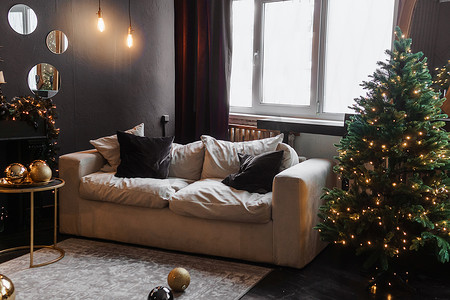 室内圣诞树摄影照片_圣诞室内有一棵美丽的圣诞树、沙发、灯泡和深色背景。