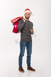圣诞节概念-年轻英俊的胡子男子拿着一杯香槟和购物袋，脸上表情快乐。