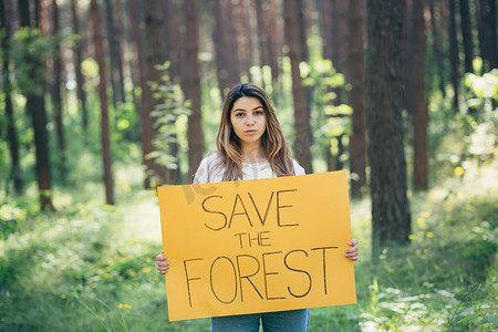 森林里年轻漂亮的女志愿者活动家，张贴着拯救森林的海报