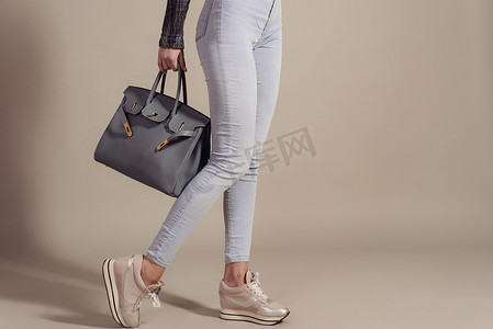 购物概念。穿着牛仔裤和运动鞋的女孩拿着一个时尚的大包特写，上面有复制空间。