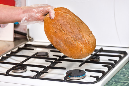 女人手拿塑料袋把面包放在煤气炉上，在家里与不同类型的细菌和病菌作斗争