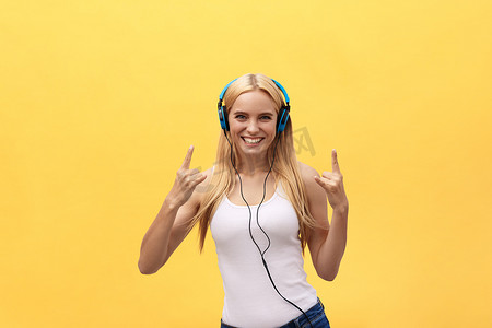 生活方式概念：一位身穿白色T恤、戴着耳机听音乐、在黄色背景下跳舞和唱歌的快乐女人的肖像