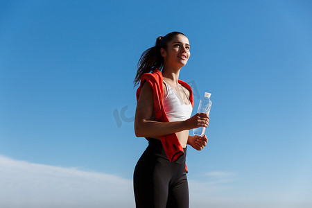 快乐自信的健身女性早上慢跑、跑步和微笑、拿着瓶水的低角度照片
