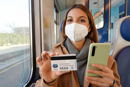 带着 FFP2 KN95 防护面罩和火车旅行的自信女人看着拿着信用卡和智能手机的相机