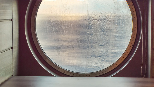 不平静的大海摄影照片_一艘海上游轮的圆形舷窗，外面喷水。